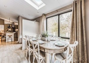 A dining area with a round wooden table set for four, surrounded by white chairs, a large window with curtains, and a skylight above. - 2 bedroom accommodation in Bridgnorth (Bridgnorth)