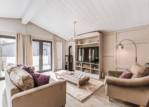 A spacious living room with a sofa, ottoman, and armchair, a fireplace, TV, and a chandelier. - 2 bedroom accommodation in Bridgnorth (Bridgnorth)