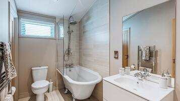 Une salle de bain moderne avec une baignoire sur pieds, des toilettes, un lavabo avec un miroir et une fenêtre avec des stores.