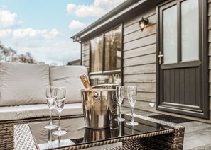 Une table en osier avec un seau à champagne et quatre verres, un canapé et, en arrière-plan, un bâtiment doté de grandes fenêtres.
