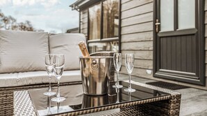 A wicker table with a champagne bucket and four glasses, a sofa, and a building with large windows in the background.