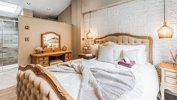 A bedroom with a large bed, a vanity with a mirror, and a wall with intricate paneling.