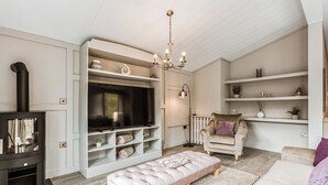 A living room with a TV, sofa, ottoman, chandelier, and shelves.