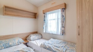 Un dormitori amb dos llits, una finestra amb cortines, una prateleira de fusta i un armari.