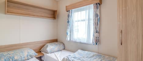 Une chambre avec deux lits, une fenêtre avec des rideaux, une étagère en bois et une armoire.