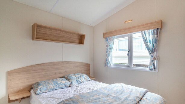 Un dormitorio con cama, cabecera de madera, ventana con cortinas y estante fijado a la pared.