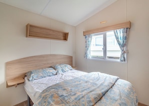 Un dormitorio con cama, cabecera de madera, ventana con cortinas y estante fijado a la pared.