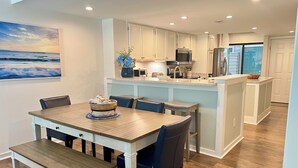 Une cuisine moderne avec des meubles blancs, un îlot central et un coin repas comprenant une table et des chaises en bois.