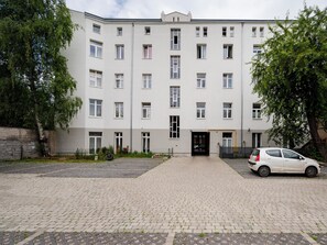 A multi-story building with a central entrance, a paved driveway, and a parked car. - Poznańska Comfy Studio (Łódź)