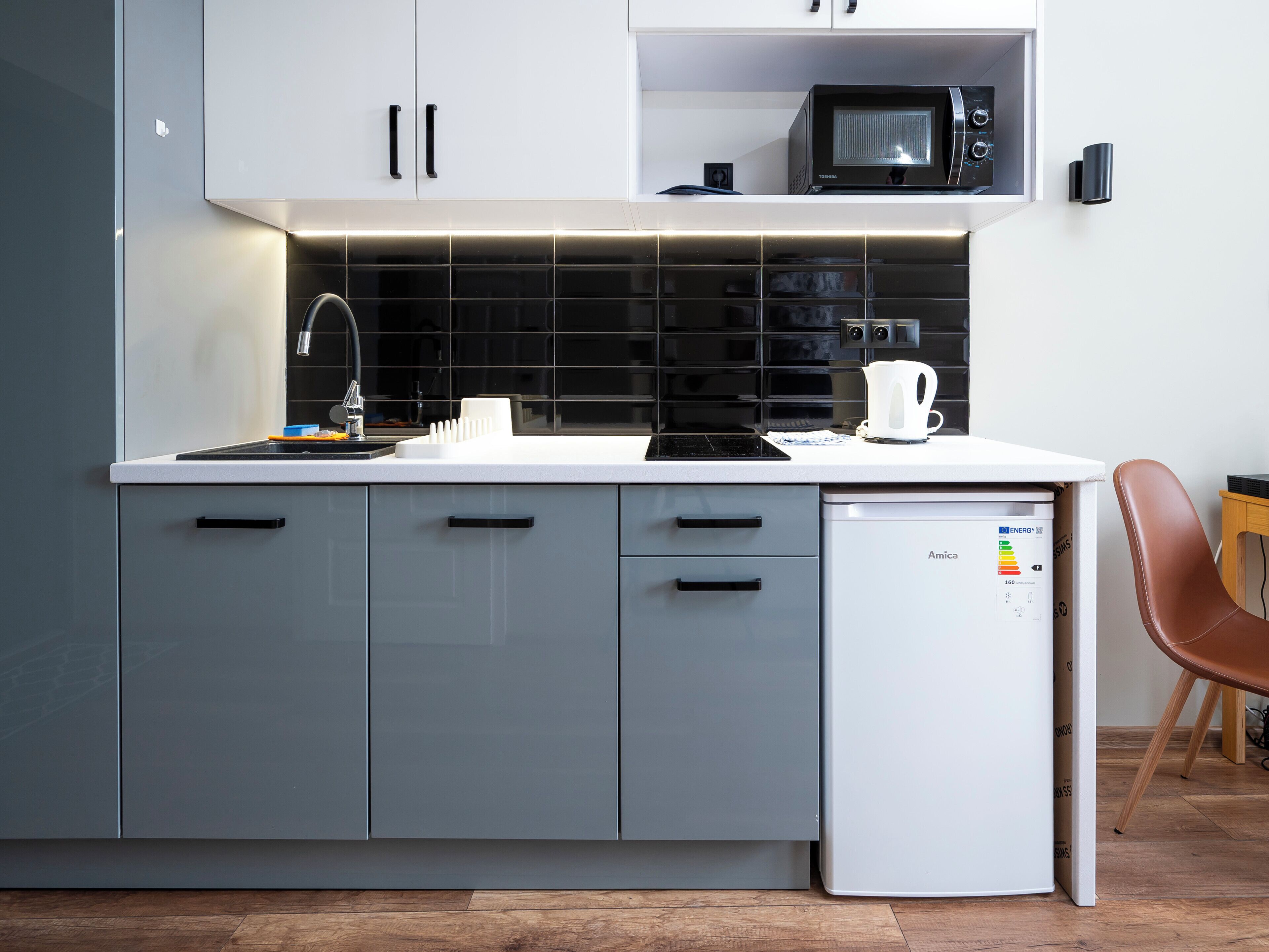 Une cuisine moderne avec des meubles gris, un plan de travail blanc, un four à micro-ondes, une machine à café et un réfrigérateur compact.