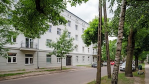Un immeuble résidentiel doté de nombreuses fenêtres et de balcons, une rue pavée et des arbres bordant le trottoir.