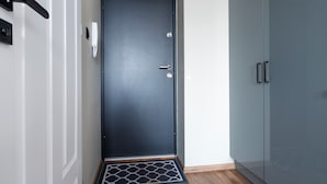 Une porte moderne de couleur sombre, dotée d’une poignée en métal et d’un trou de serrure, un petit paillasson à sa base et une porte vitrée sur le côté droit.