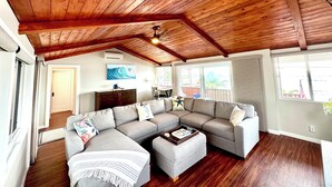 Ein geräumiges Wohnzimmer mit einer großen Eckcouch, einer Holzbalkendecke und Blick ins Freie.