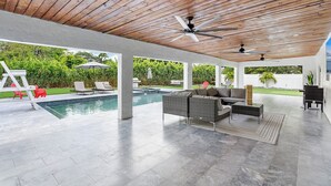 Un espacio al aire libre techado con piscina, asientos y ventiladores de techo.