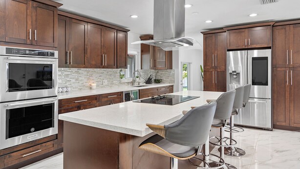 Cocina moderna con electrodomésticos de acero inoxidable, armarios de madera y una isla central con taburetes de bar.