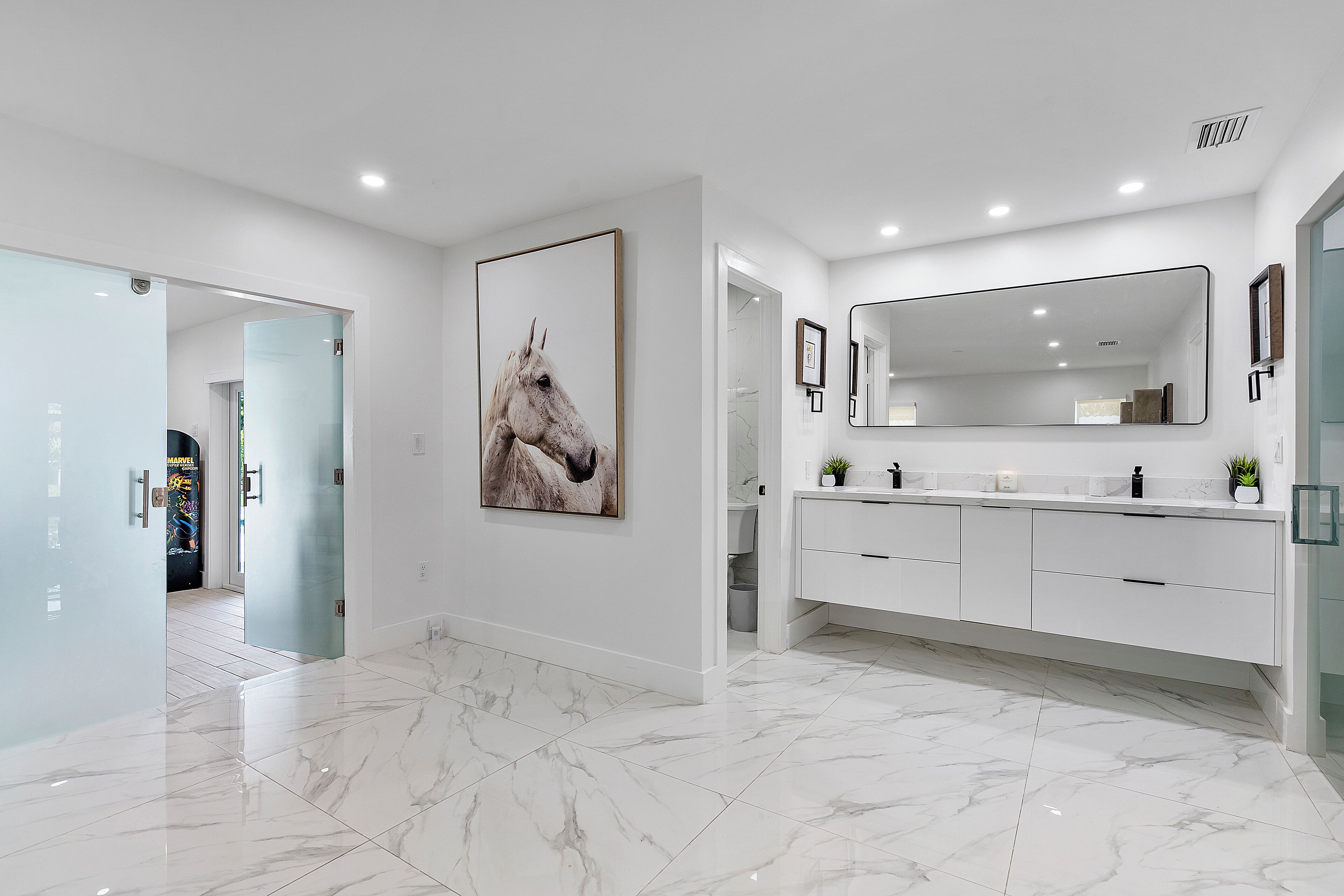 Un bagno moderno con uno specchio grande, pavimenti in marmo e un quadro raffigurante un cavallo.