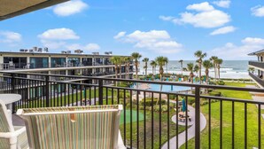 A balcony with a view of a pool, palm trees, and the ocean. - About the View at Ocean House 312 (St. Augustine)