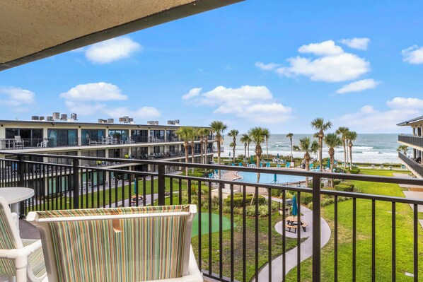 A balcony with a view of a pool, palm trees, and the ocean.