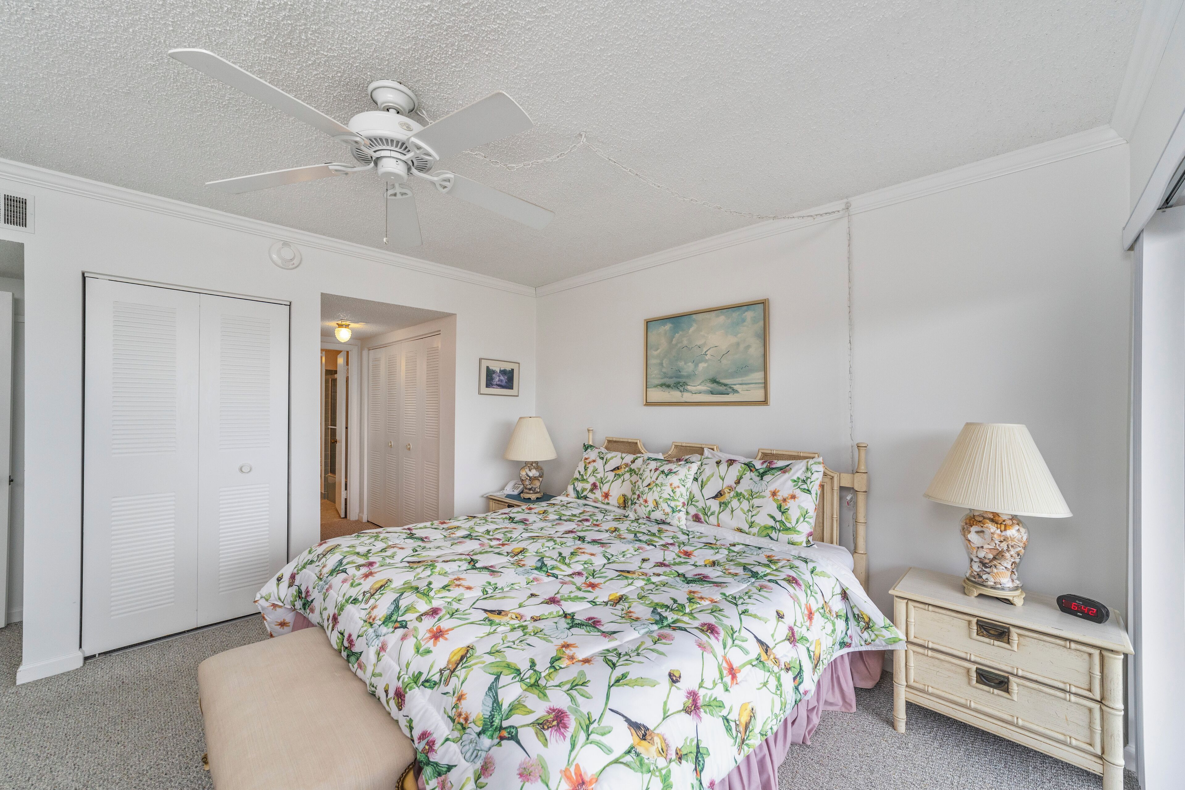 A bedroom with a bed, bedside tables, a ceiling fan, and a nightstand with a lamp.