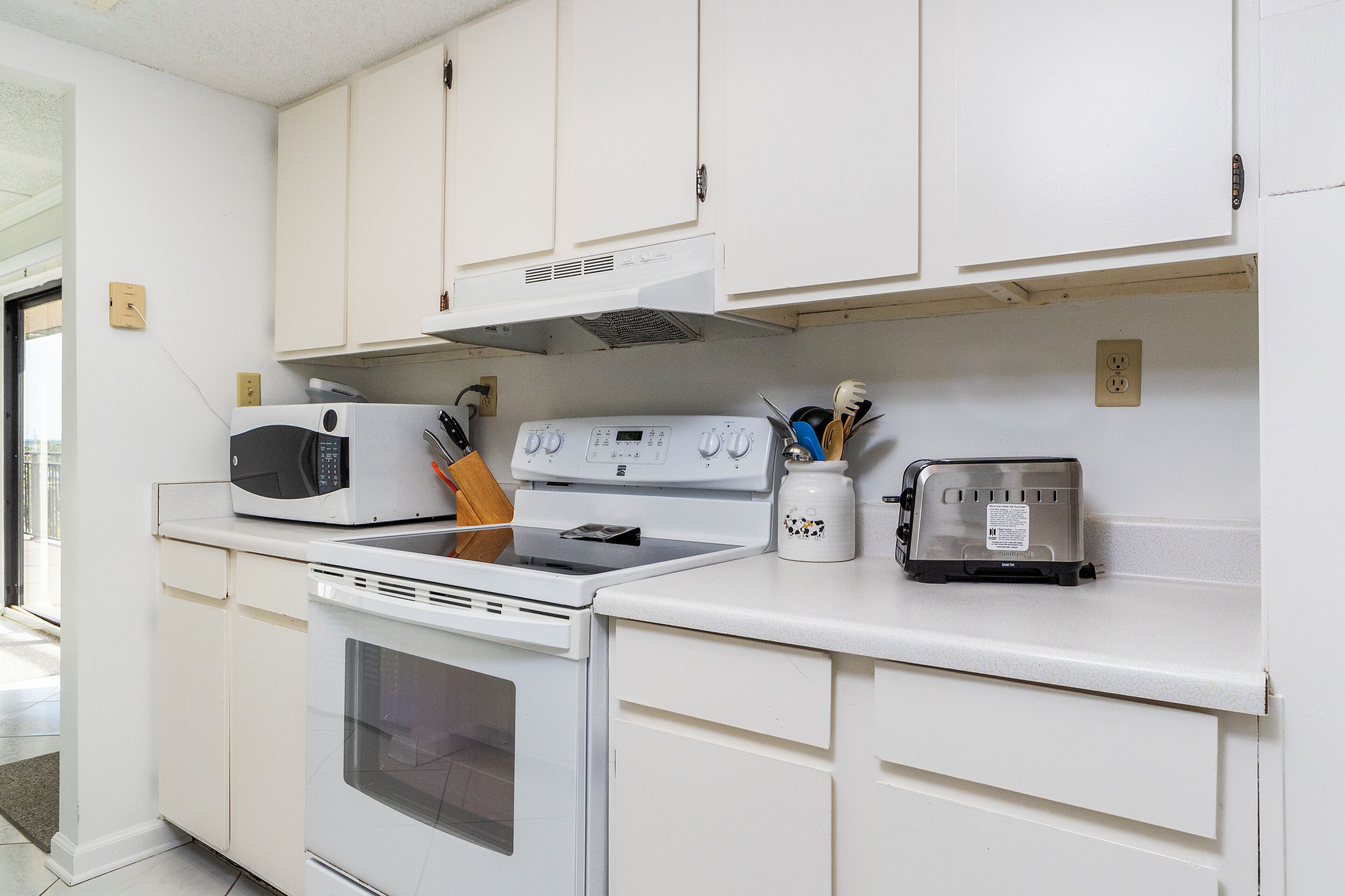 A kitchen with white cabinets, a microwave, an oven, a toaster, and a spice rack.