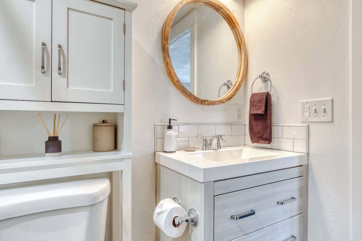 A bathroom with a white sink, a mirror with a wooden frame, a towel rack, and a toilet paper holder.