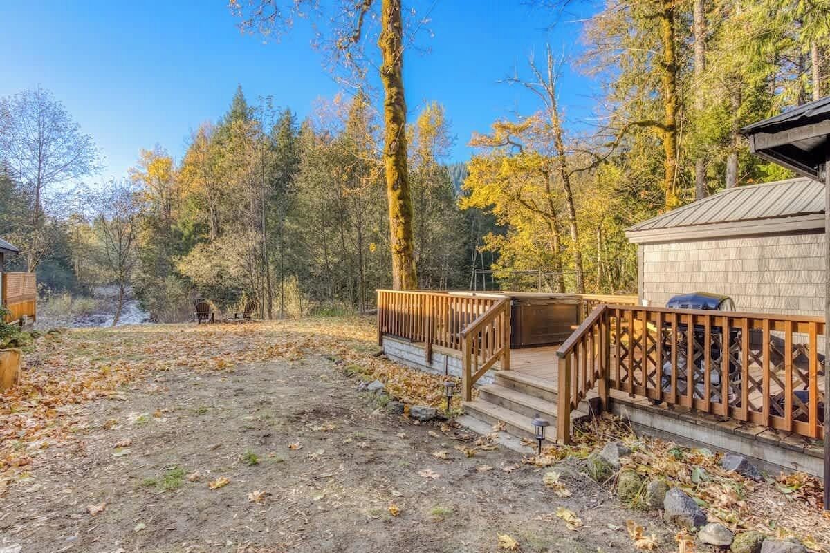 Une cabane dotée d’une terrasse en bois et d’un mur en pierre, entourée d’une forêt aux couleurs automnales.