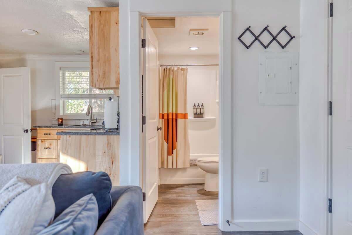 A modern kitchen with wooden cabinets, a countertop, and a window. There is a bathroom with a shower curtain and a toilet.