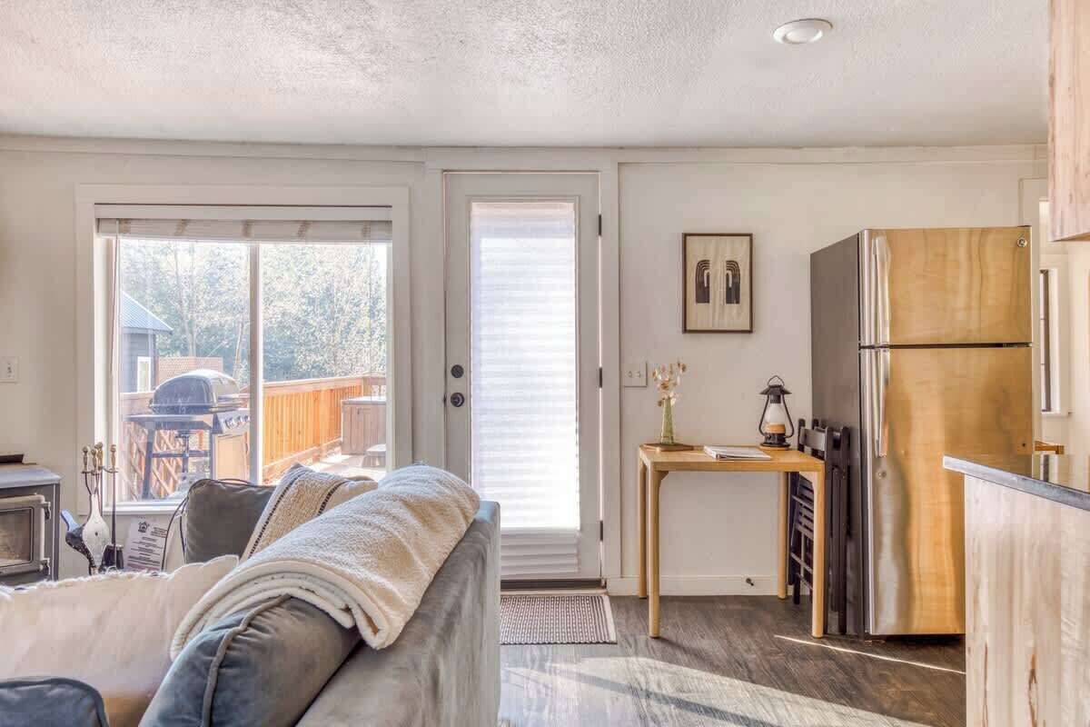 A cozy living room with a sofa, a small table with a lamp, and a kitchen area with a refrigerator.