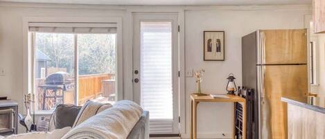 A cozy living room with a sofa, a small table with a lamp, and a kitchen area with a refrigerator.