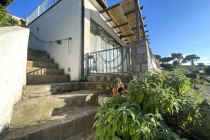 A building with a white exterior, a set of stone steps leading to a door, and a metal railing. - Nettuno Apartment (Capoliveri)