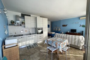 A compact kitchen with white cabinets, a dining table with a checkered tablecloth, and a television on a wooden stand.