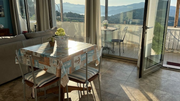 A dining area with a table, chairs, and a view of mountains through large windows. - Nettuno Apartment (Capoliveri)