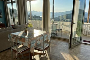 A dining area with a table, chairs, and a view of mountains through large windows. - Nettuno Apartment (Capoliveri)