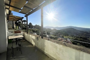 Un balcone con tavolo e sedie, affacciato su un panorama suggestivo con montagne e cielo sereno.