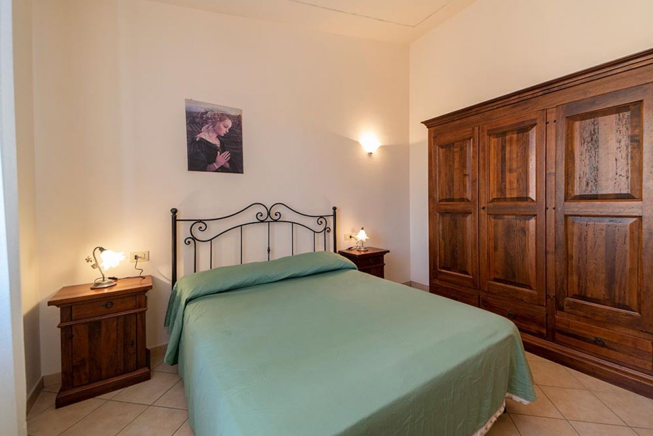 A bedroom with a bed, wooden nightstands, a wall-mounted light, a wardrobe, and a framed picture on the wall.