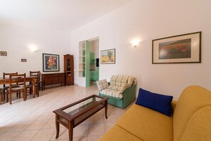 Una sala de estar con un sofá, una mesa de centro, una mesa de comedor con sillas y un armario verde.