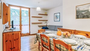 A dining area with a wooden table set for four, a checkered tablecloth, and a view of the outdoors through a large window. - Beautiful apartment for 4 guests with WIFI, TV and balcony (Canazei)