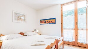 A bedroom with a wooden bed, white bedding, a nightstand with a lamp, and a painting on the wall. - Beautiful apartment for 4 guests with WIFI, TV and balcony (Canazei)