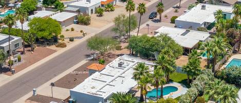 Une vue aérienne d’un quartier résidentiel composé de plusieurs maisons, chacune ayant un toit plat, une piscine et étant entourée de palmiers.