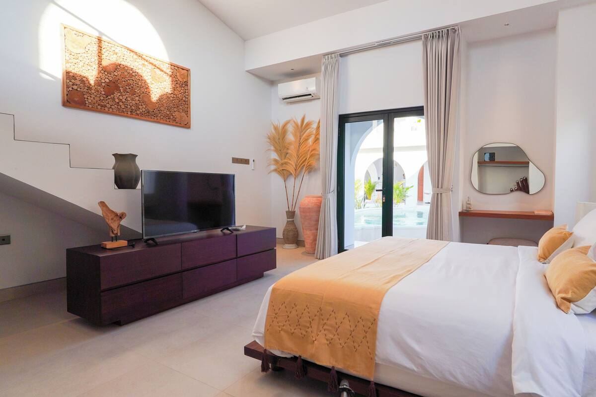 Quarto moderno com cama, televisão sobre cômoda e vista para uma piscina ao ar livre.