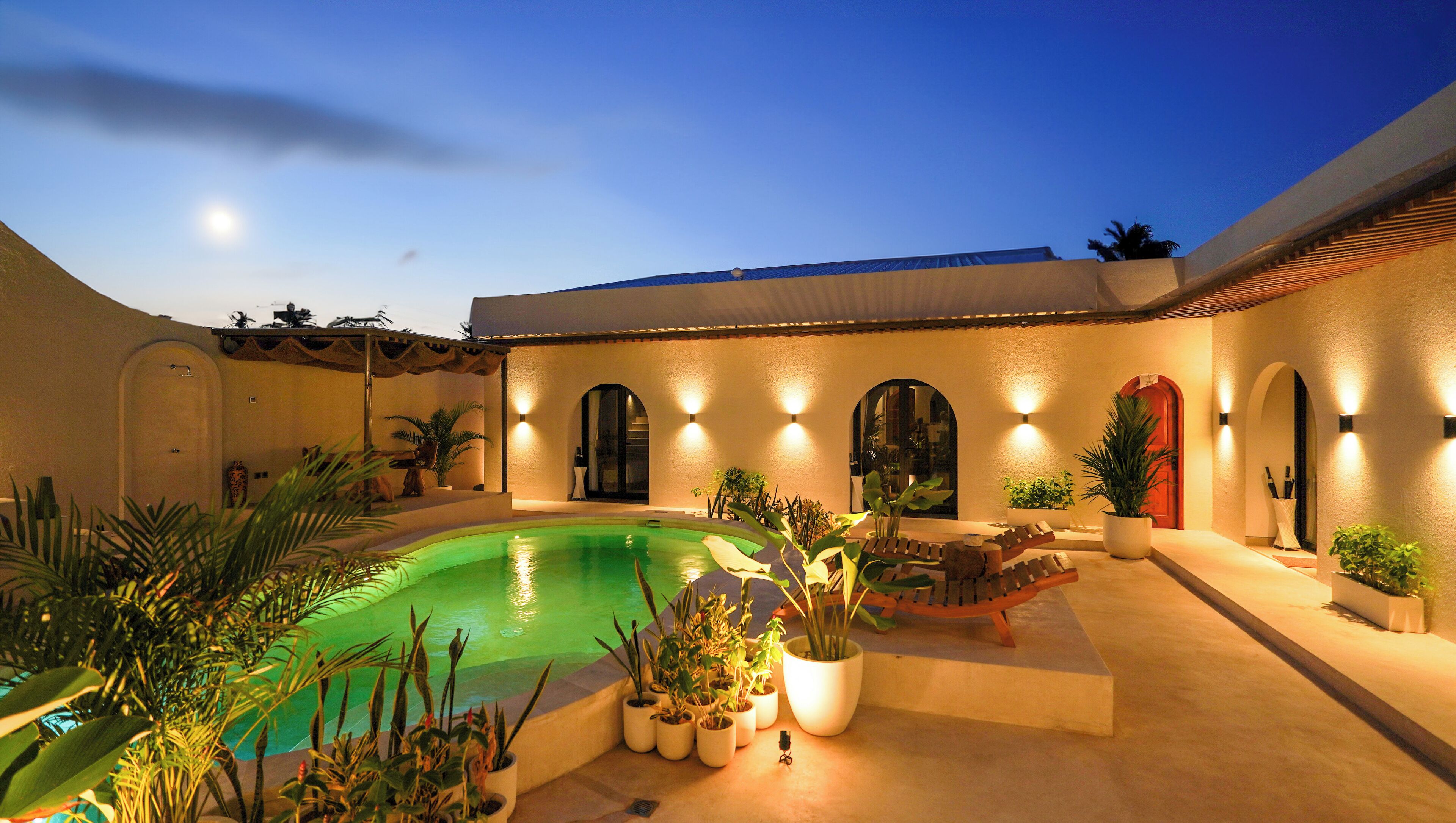 A courtyard with a swimming pool, potted plants, and a building with arched doorways and walls.