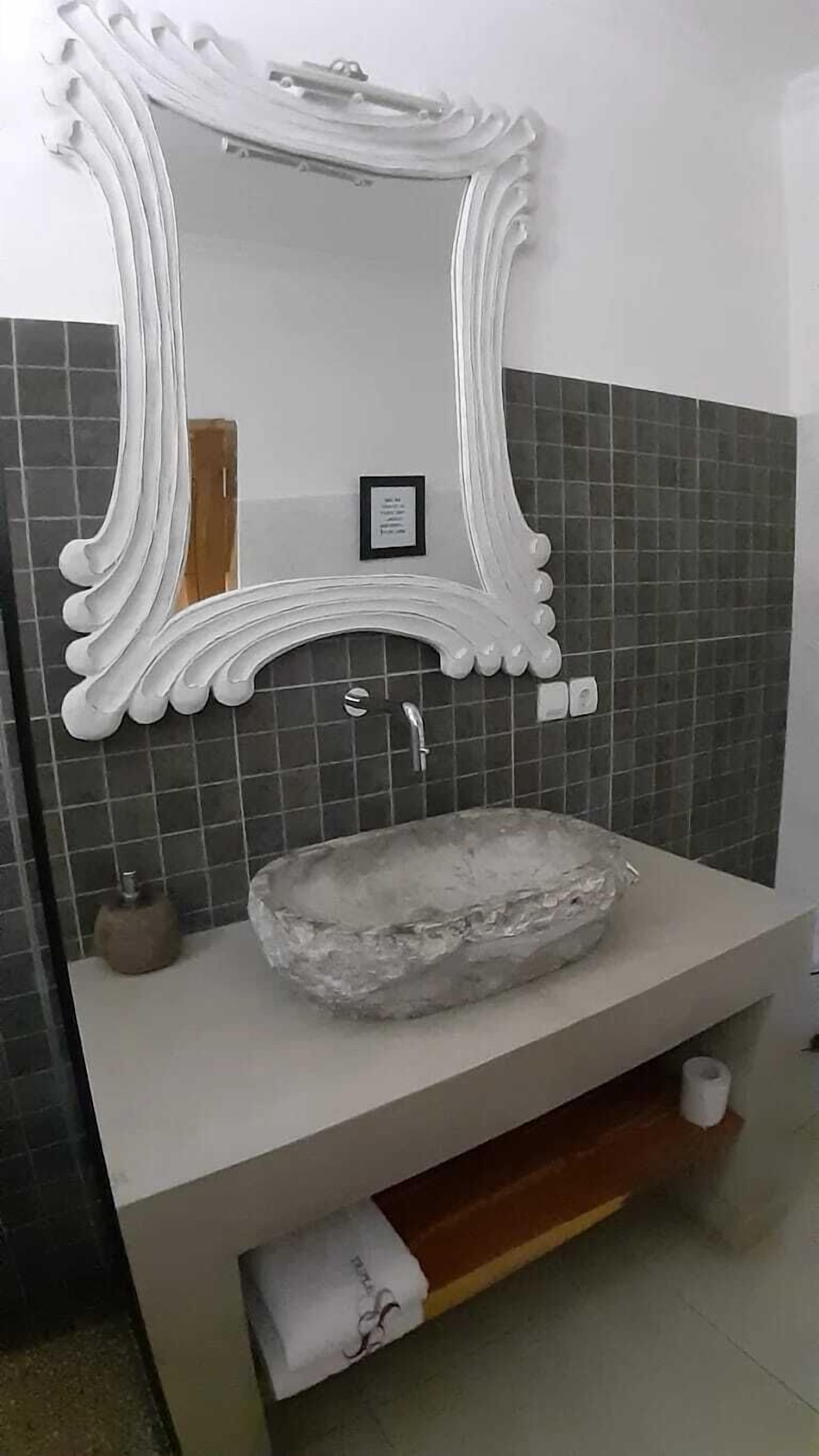 A bathroom with a white vanity, a marble sink, and a decorative mirror with a scalloped frame.