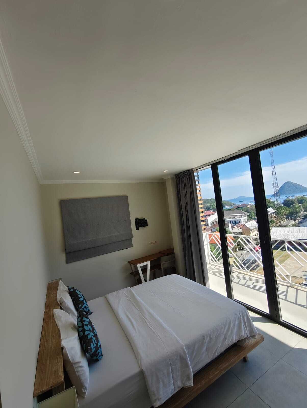 A modern hotel room with a bed, a desk, and a large window offering a city view.