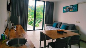 A modern kitchen with a wooden countertop, a sink, and a dining area with a table and chairs. There is a sofa with cushions and a painting on the wall. - Triple 888  Suites (Labuan Bajo)
