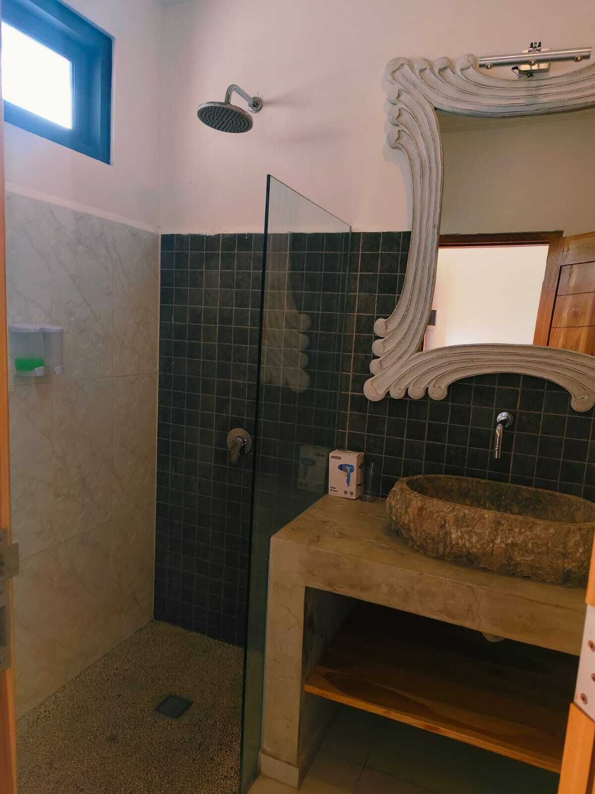A bathroom with a glass shower enclosure, a freestanding sink with a stone basin, and a decorative mirror.