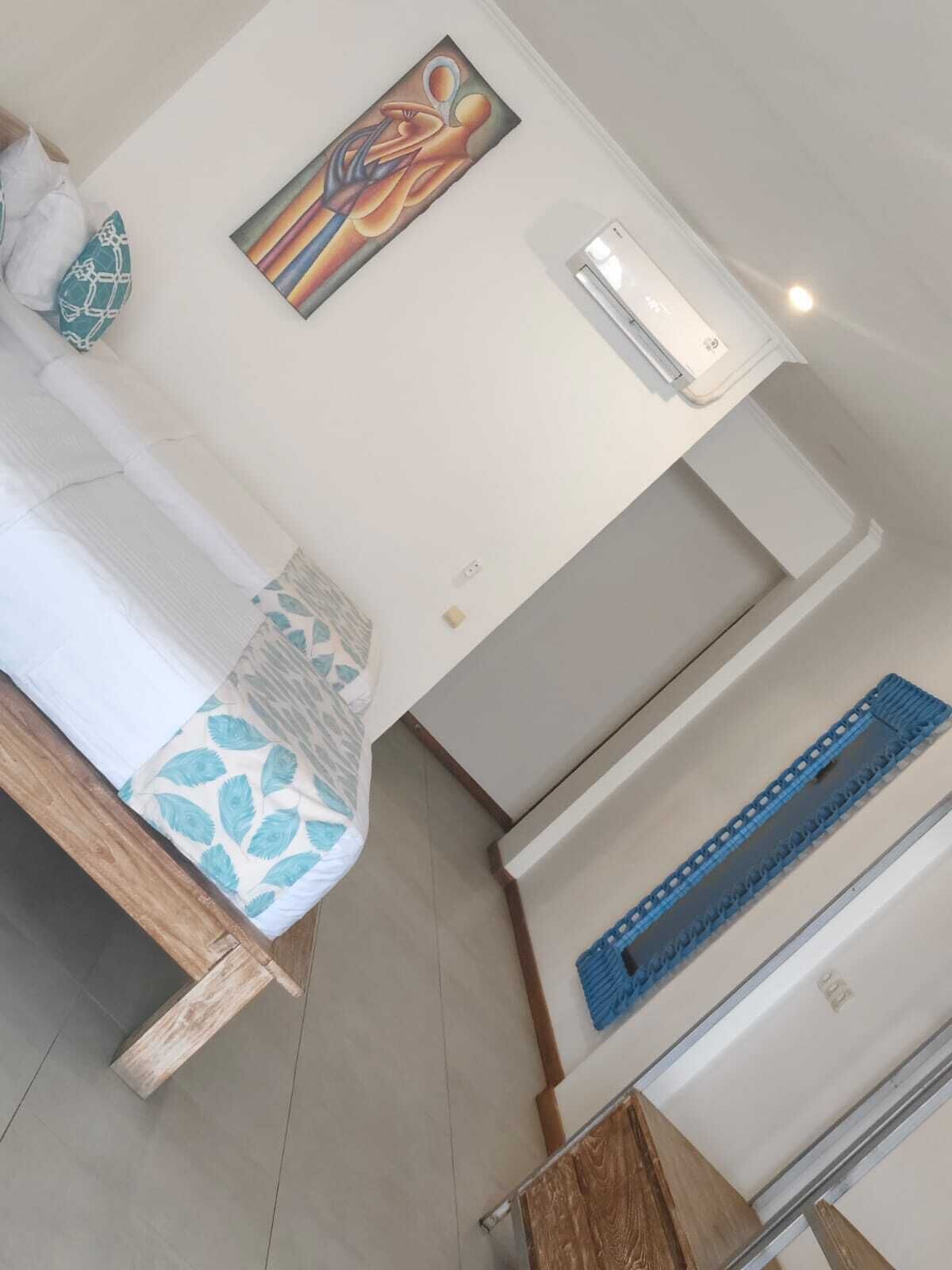 A room with a bed, a painting, an air conditioning unit, and a wooden bench.