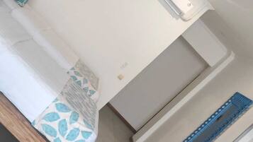 A room with a bed, a painting, an air conditioning unit, and a wooden bench.