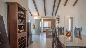 Een moderne keuken met houten balken, een centraal eiland en een eetgedeelte met een glazen tafel en stoelen.