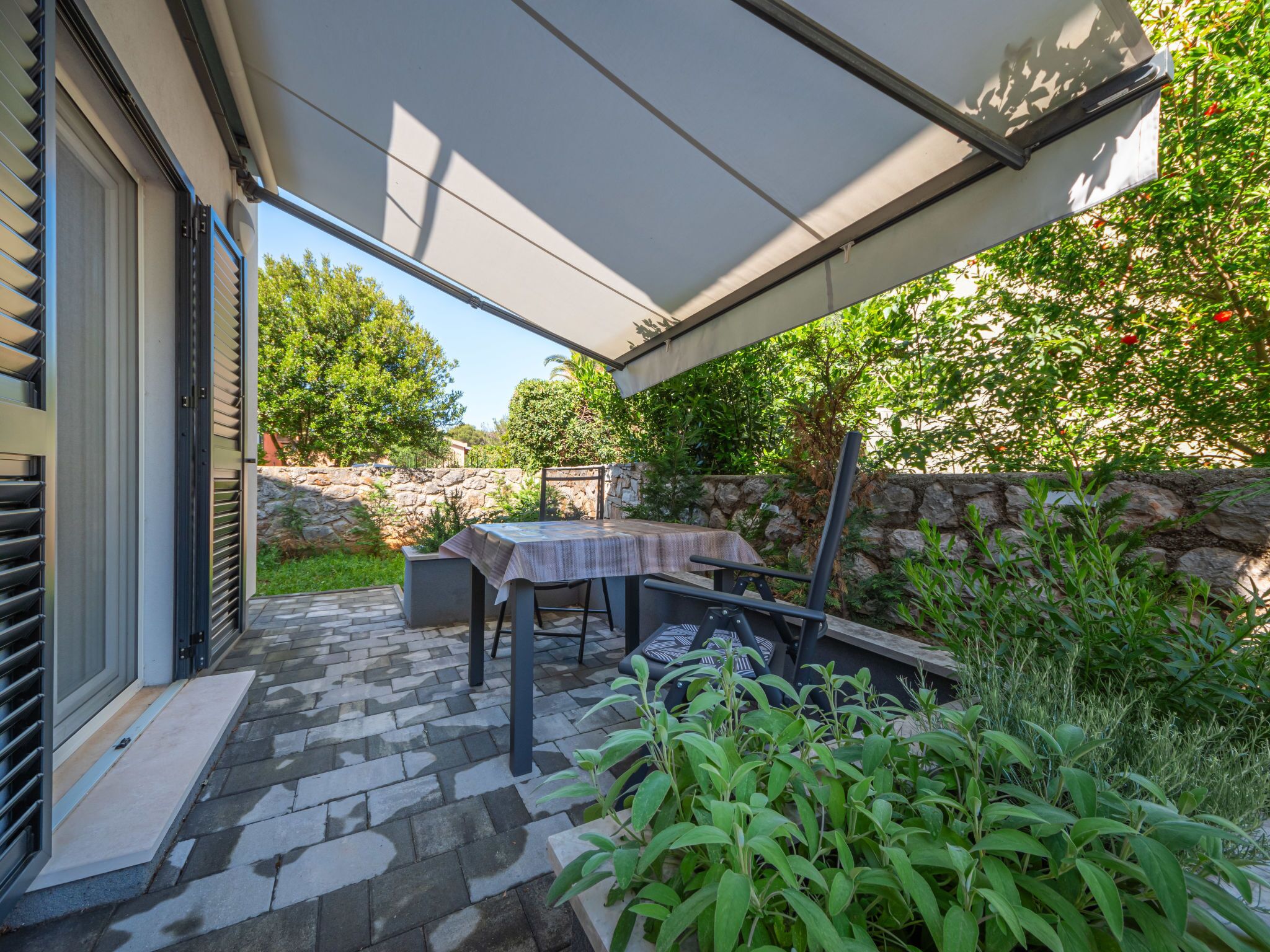 An outdoor patio with a table and chairs, a stone wall, and greenery.