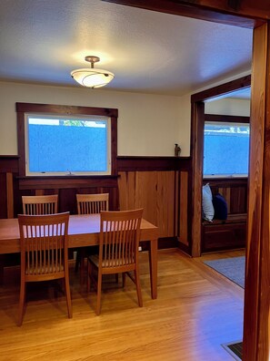 Un coin repas avec une table et des chaises en bois, un luminaire au plafond et deux fenêtres à vitres dépolies.
